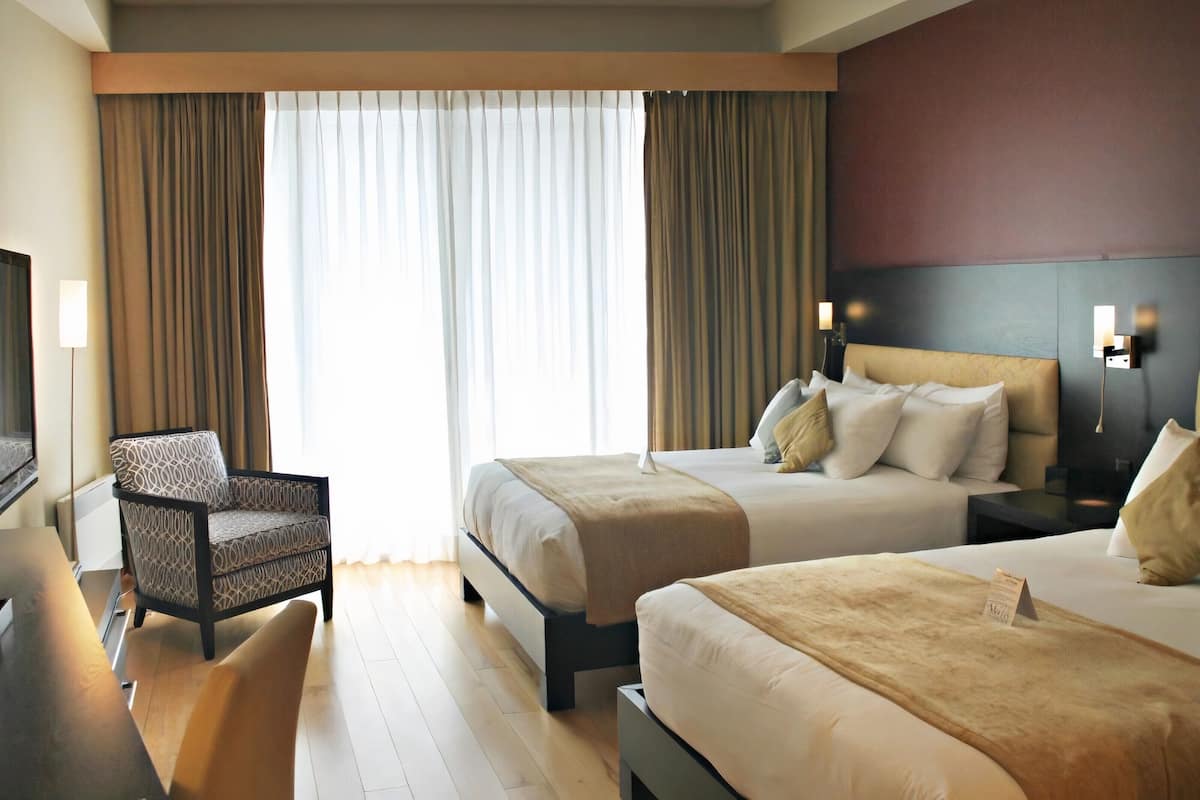 Habitación de hotel con dos camas, un sofá, un televisor y un ventanal con cortinas.