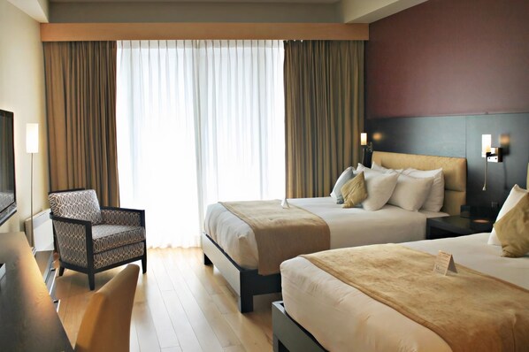 Habitación de hotel con dos camas, un sofá, un televisor y un ventanal con cortinas.