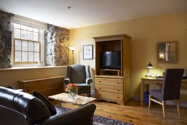 A living room with a stone wall, wooden furniture, a television, and a window with natural light.
