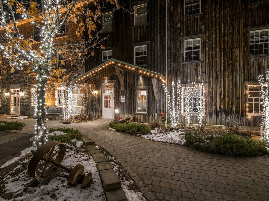 Un bâtiment rustique à la façade en bois, illuminé par des guirlandes lumineuses, et un chemin pavé menant à l’entrée.
