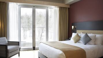 Ein Hotelzimmer mit einem großen Bett, einem Sessel und einer Schiebeglastür, die auf einen Balkon führt.