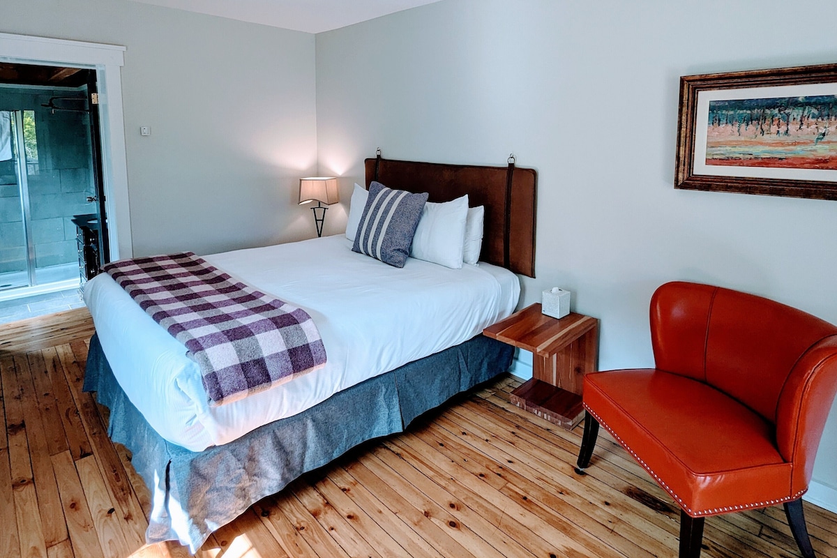 Un dormitorio con una cama, una mesita de noche, una silla y un cuadro en la pared.