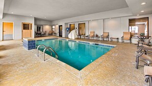 Un espace piscine doté d’un sol carrelé, d’une piscine avec un escalier en métal, ainsi que de plusieurs chaises longues et tables.