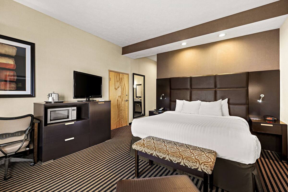 A hotel room with a large bed, a desk with a television, a chair, and a microwave.