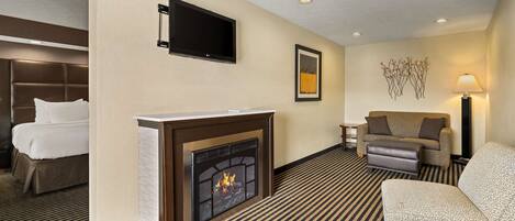 A hotel room with a fireplace, a bed, a sofa, and a TV mounted on the wall.