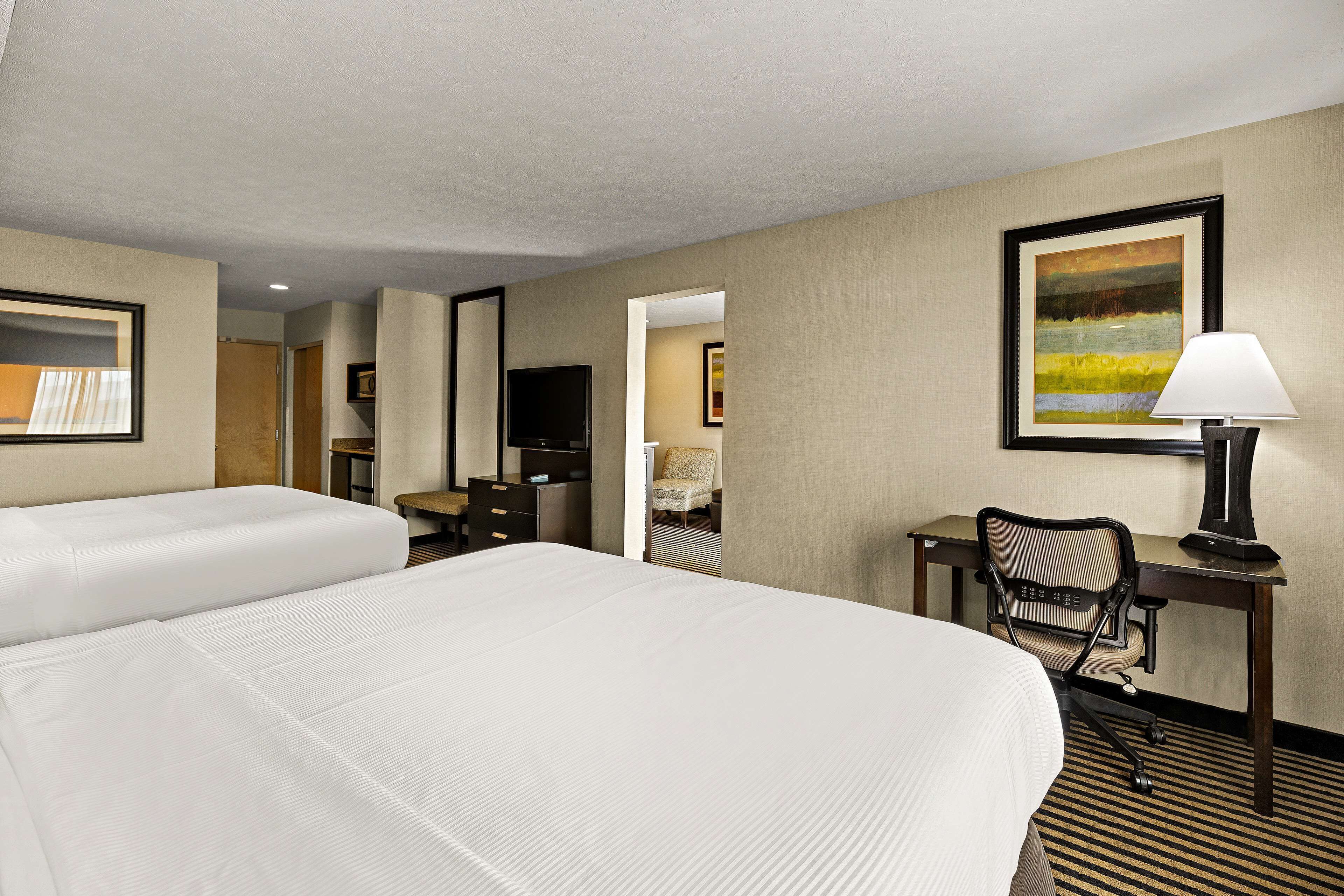 A hotel room with two beds, a desk with a chair, a TV, and a painting on the wall.