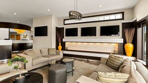 Un salon moderne comprenant un canapé, un pouf et une table basse, un téléviseur à écran plat fixé au mur et un vase décoratif.