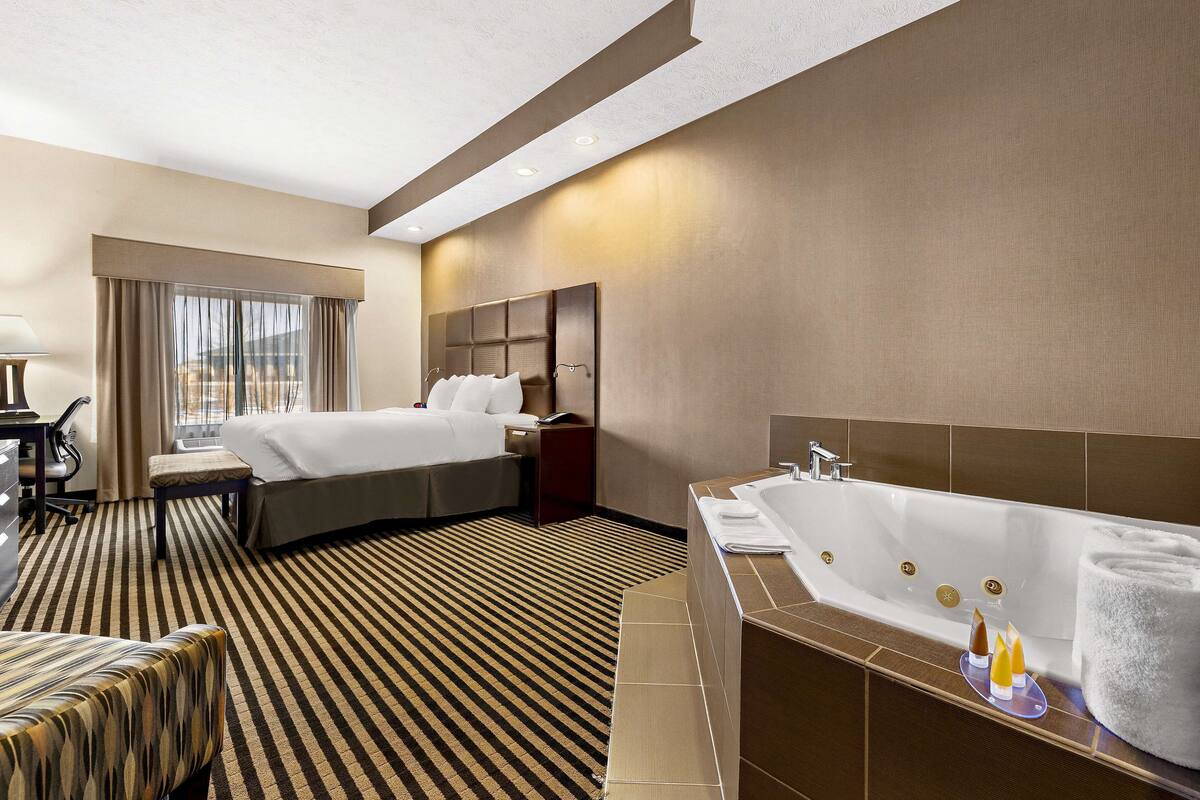 A hotel room with a large bed, a separate sitting area, a bathtub, and a desk with a chair.