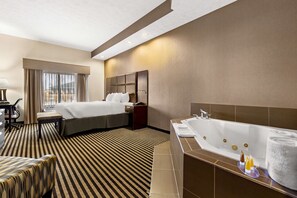 A hotel room with a large bed, a separate sitting area, a bathtub, and a desk with a chair. - Sonesta Essential Indianapolis Airport (Plainfield)