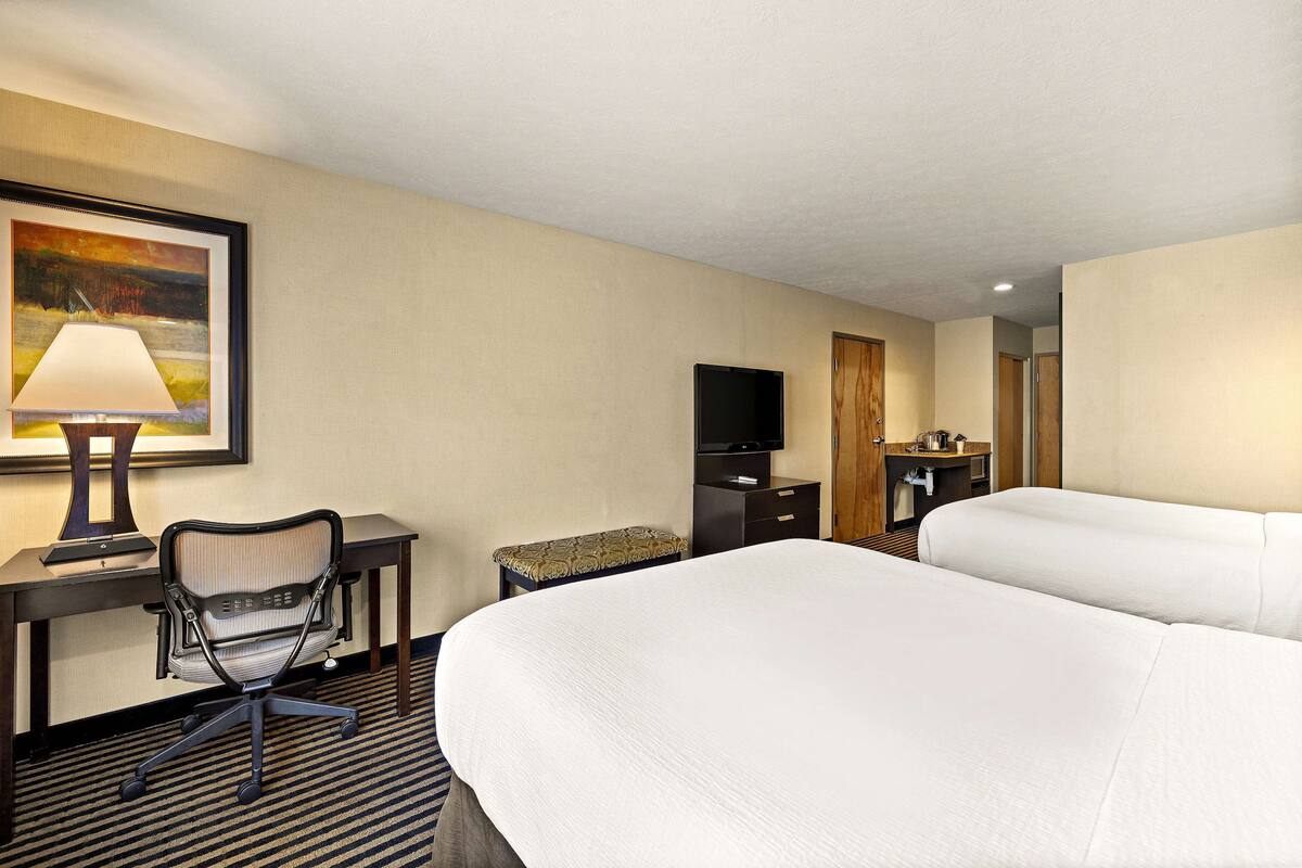 A hotel room with a large bed, a desk with a chair, a television, and a painting on the wall.