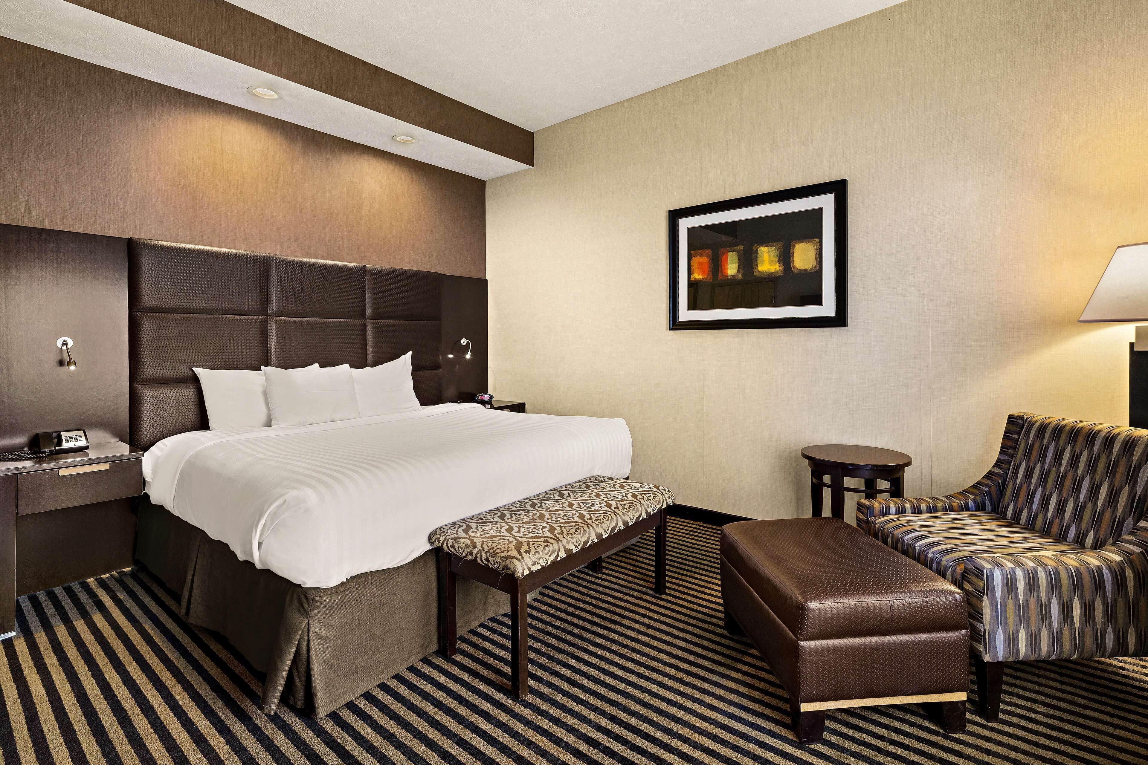 A hotel room with a large bed, a bench, a sofa, a bedside table, and a wall-mounted picture.