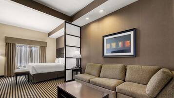 Una habitación de hotel con una cama, un sofá, una mesita de centro, una lámpara y un cuadro en la pared.