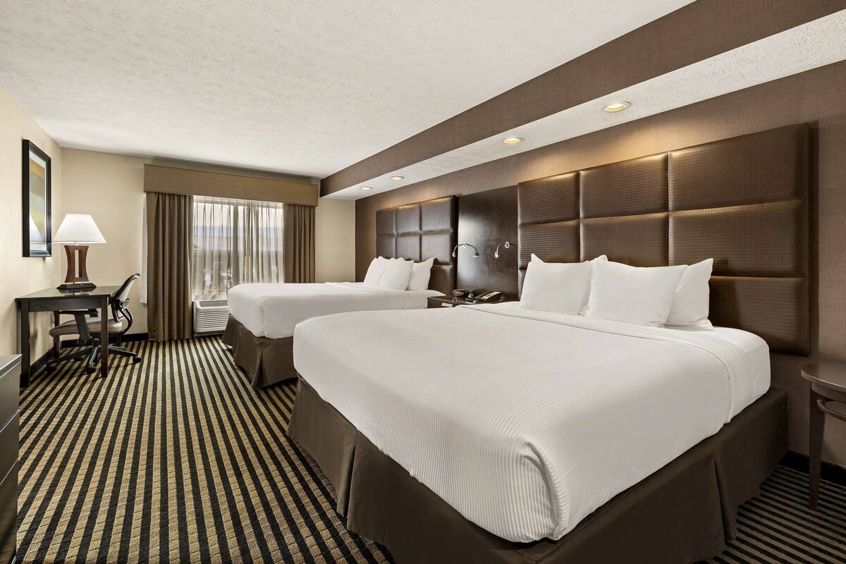 A hotel room with two beds, a desk, a chair, and a large window with curtains.