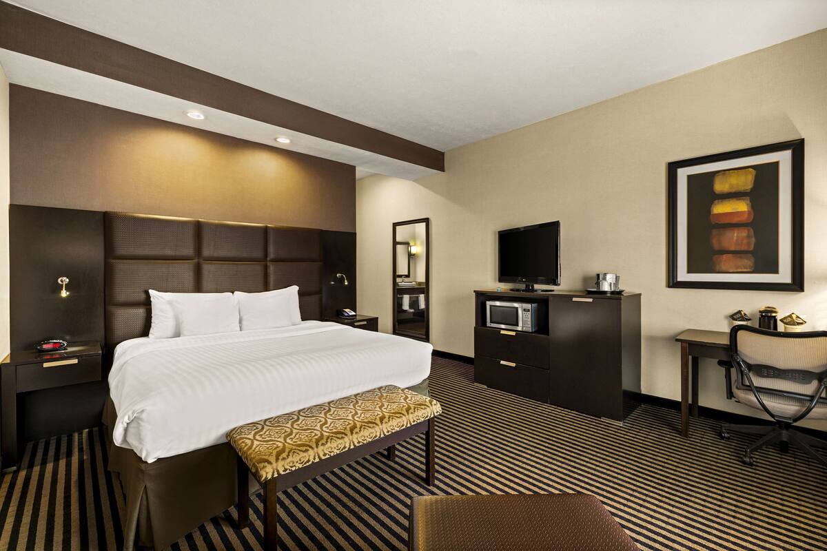 A hotel room with a large bed, a desk, a chair, a television, and a microwave.