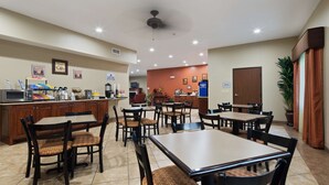 A hotel dining area with multiple tables and chairs, a coffee station, and a visible kitchen area. - Best Western Oasis Inn (Canadian)