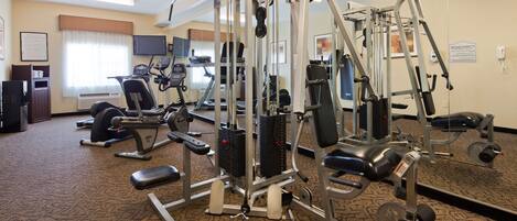 A hotel fitness center with cardio machines, weight training equipment, and a television.