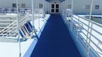 A corridor with a blue floor and white railings, leading to a door at the end.