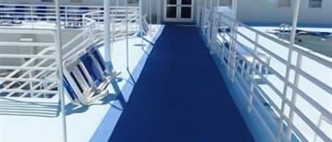 A corridor with a blue floor and white railings, leading to a door at the end.