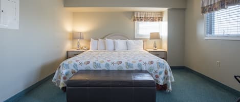 A bedroom with a bed, a bench, a window with blinds, and a wall-mounted lamp.