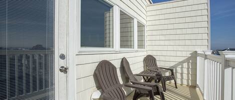 A balcony with two Adirondack chairs and a small table, overlooking a body of water.