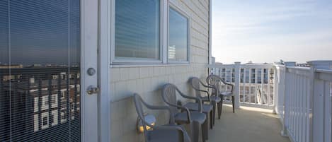 A balcony with plastic chairs and a white railing, overlooking a residential area.