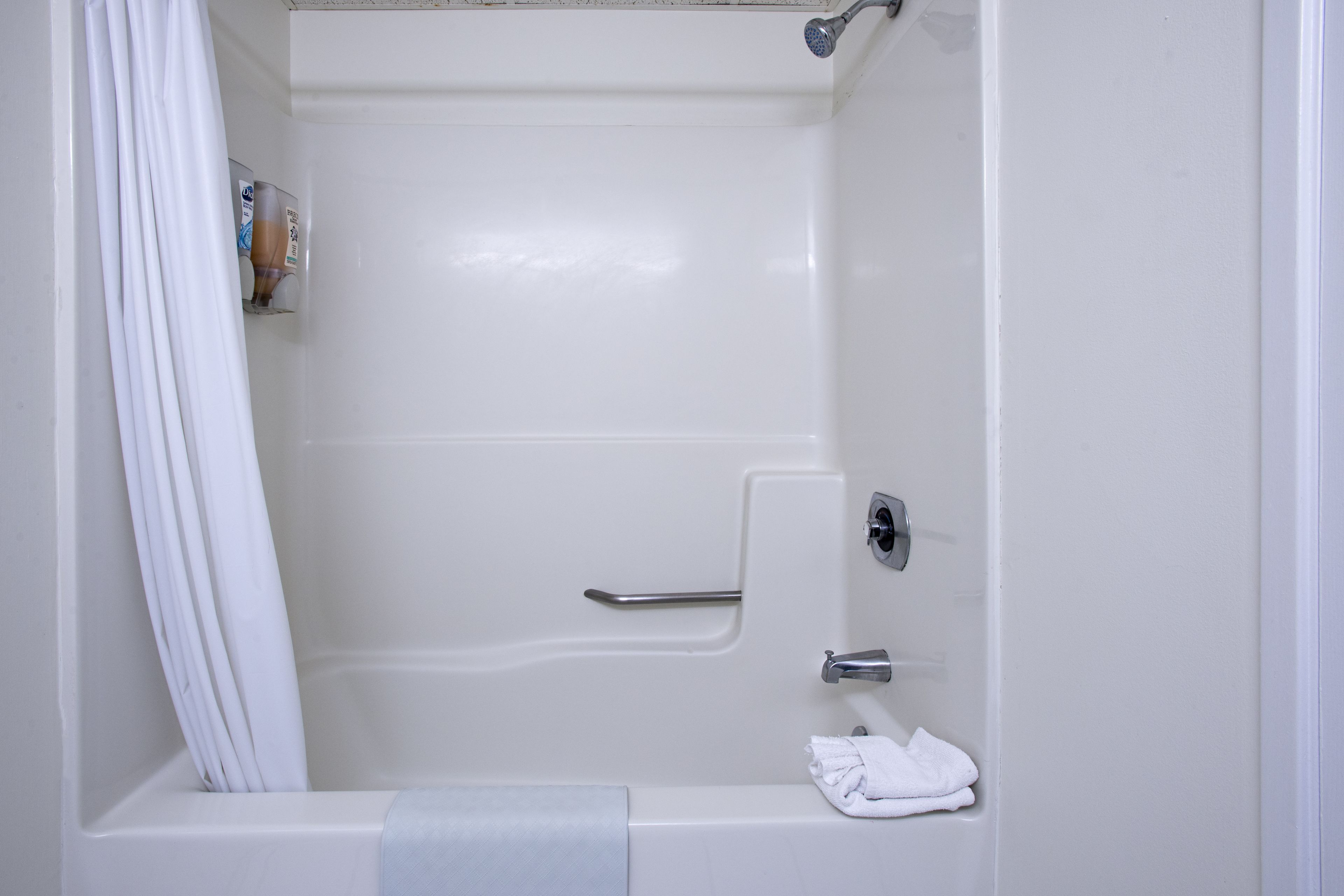 Eine weiße Badewanne mit Duschkopf, Handtuchhalter und einer Shampoo-Flasche.