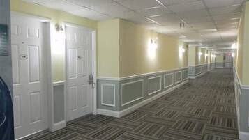 A hotel corridor with patterned carpet, white doors, and light-colored walls.