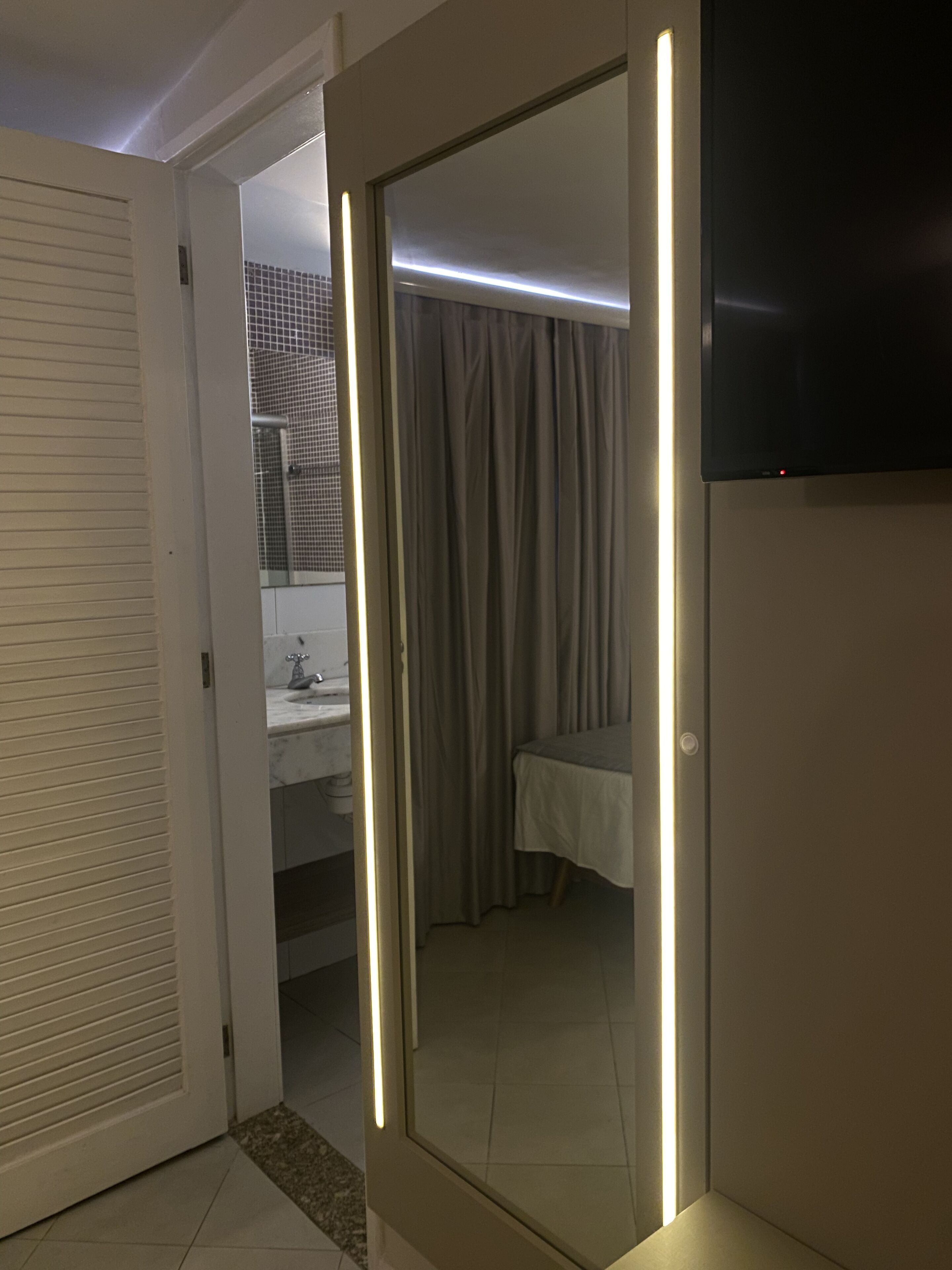 Habitación de hotel con puerta corredera que da a un baño, una cama y un televisor montado en la pared.