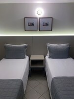 Habitación de hotel con dos camas, una mesita de noche y una lámpara fijada a la pared.