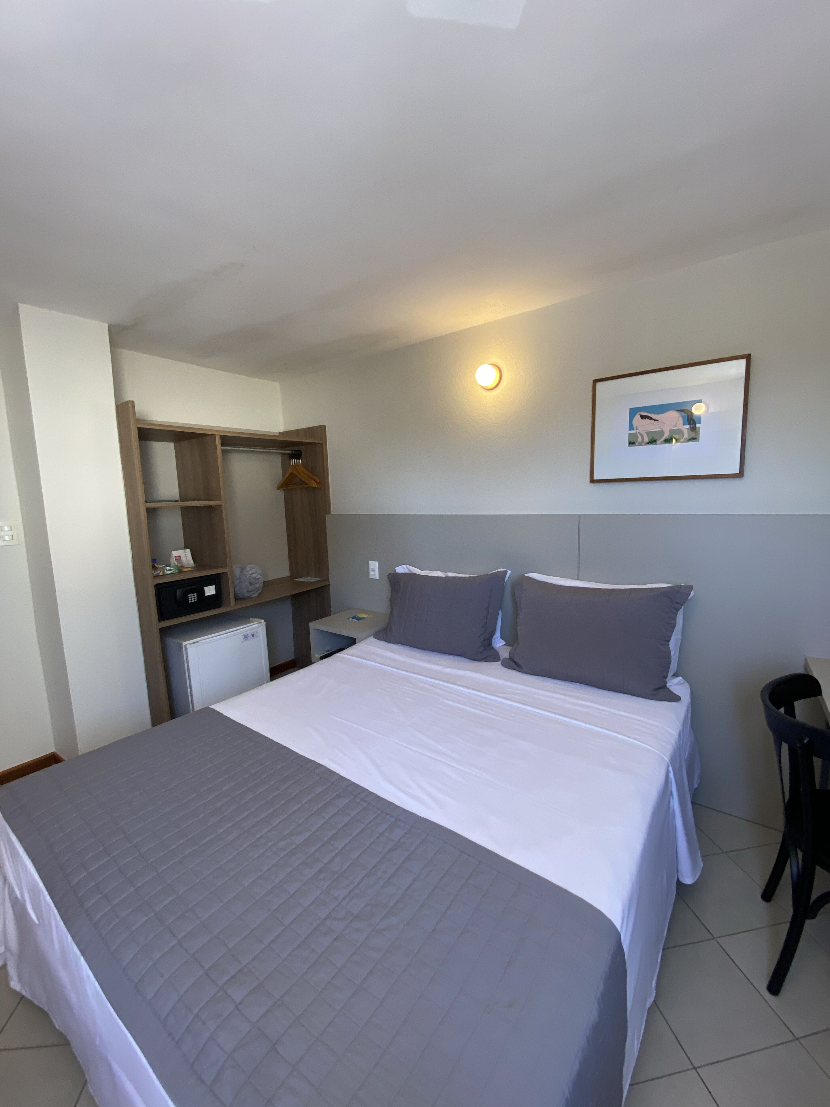 Habitación de hotel con cama, escritorio, silla, armario y un refrigerador pequeño.