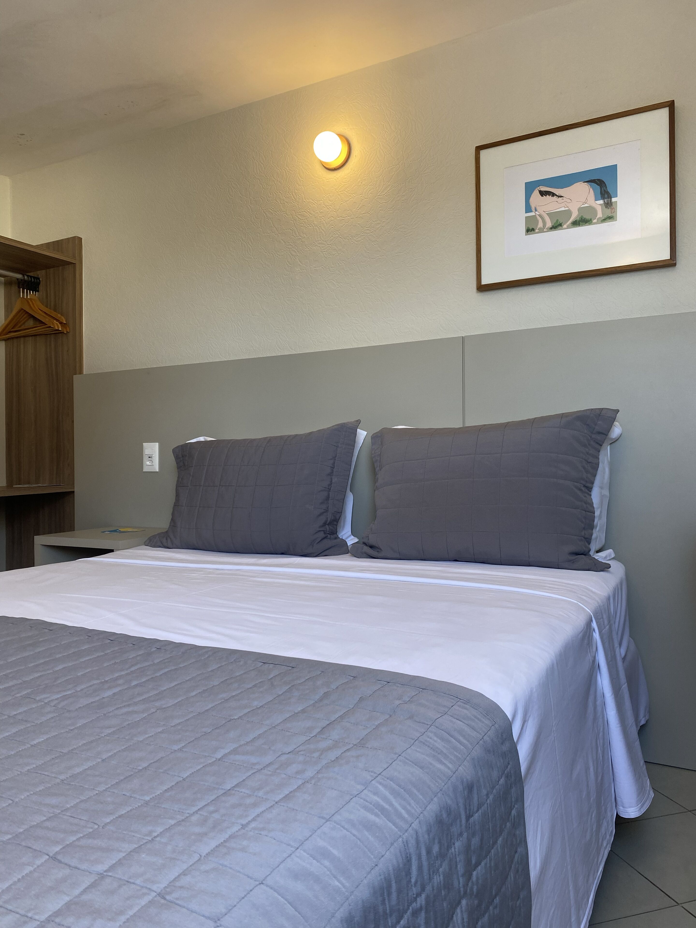 Una cama bien hecha con ropa de cama gris, cabecera y un cuadro en la pared.
