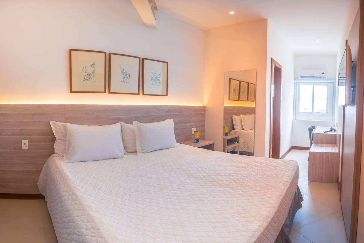 A bedroom with a large bed, a nightstand, a bedside table, and a window.