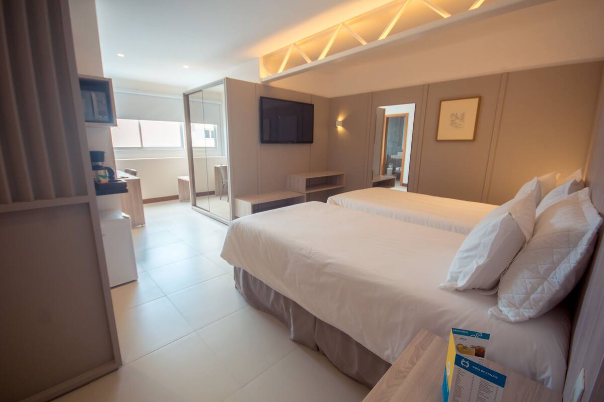 A modern hotel room with a large bed, a flat-screen TV mounted on the wall, and a glass door leading to a balcony.