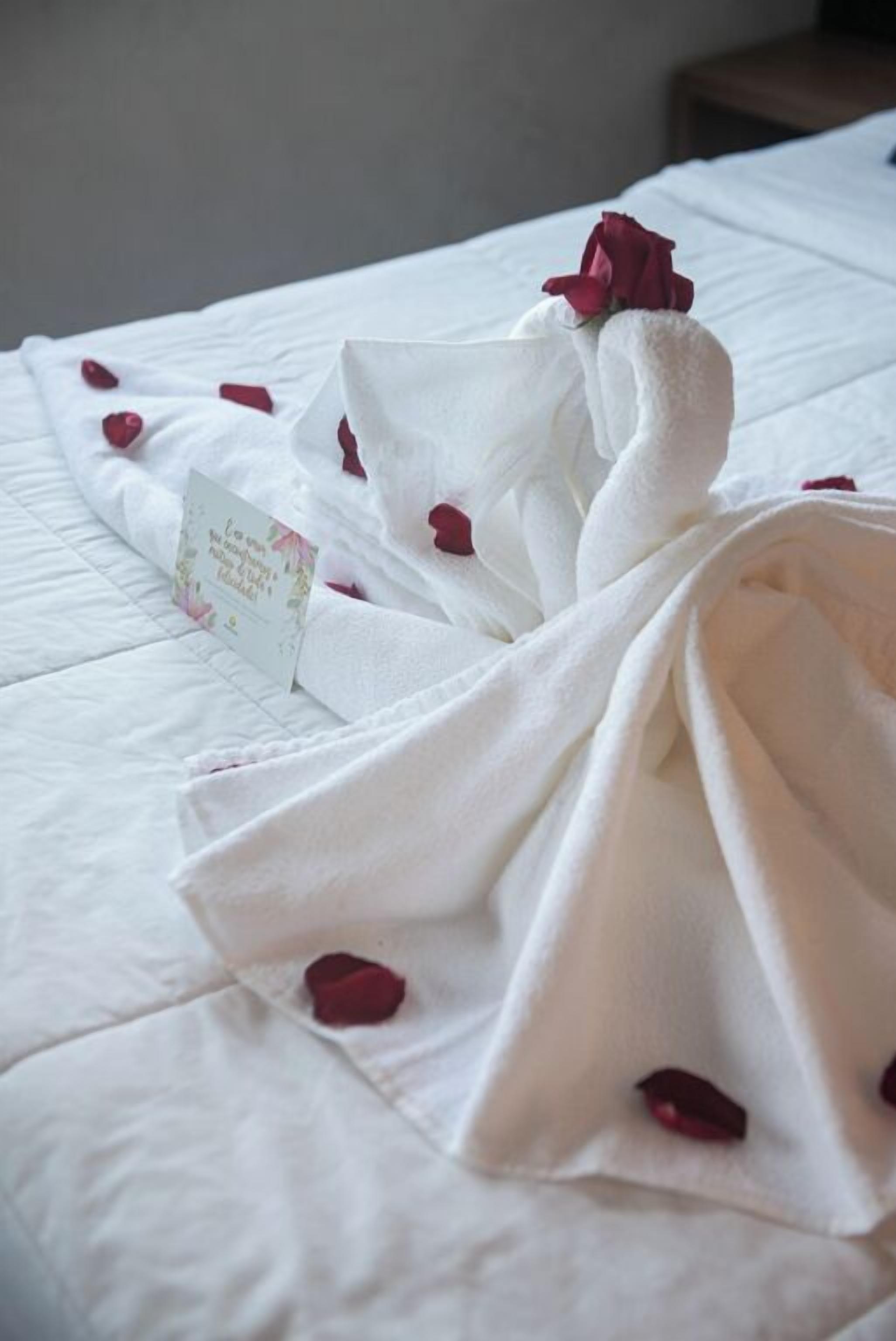 Una cama bien hecha con una rosa y una tarjeta encima.