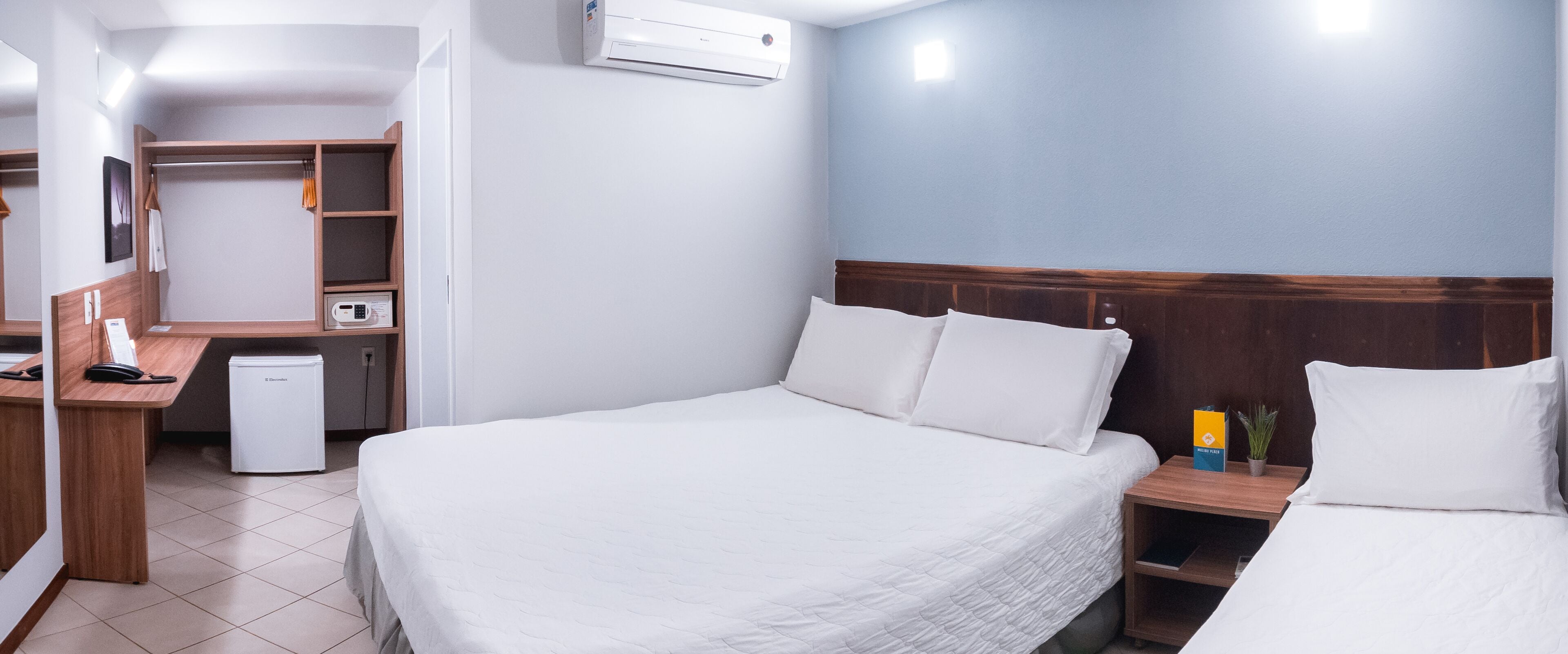 A hotel room with a bed, bedside table, and a desk with a computer and phone.