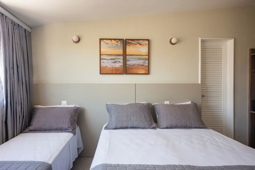 A hotel room with two beds, a large painting of a sunset, and a window with curtains.