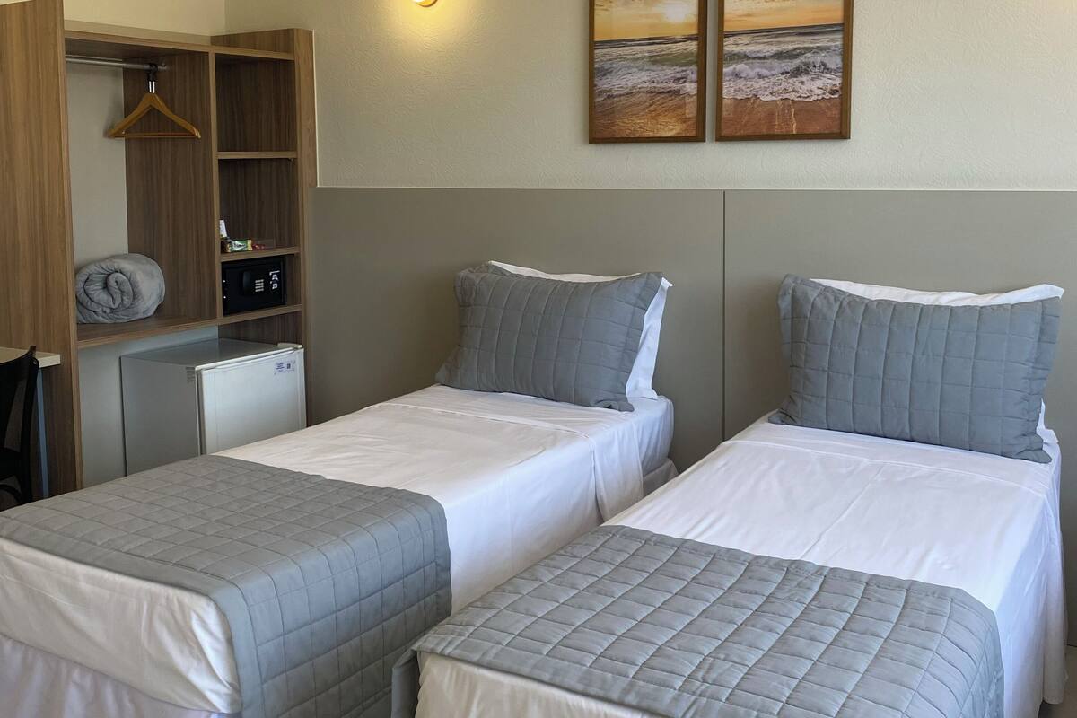A hotel room with two single beds, a wardrobe, a small desk, and a refrigerator.