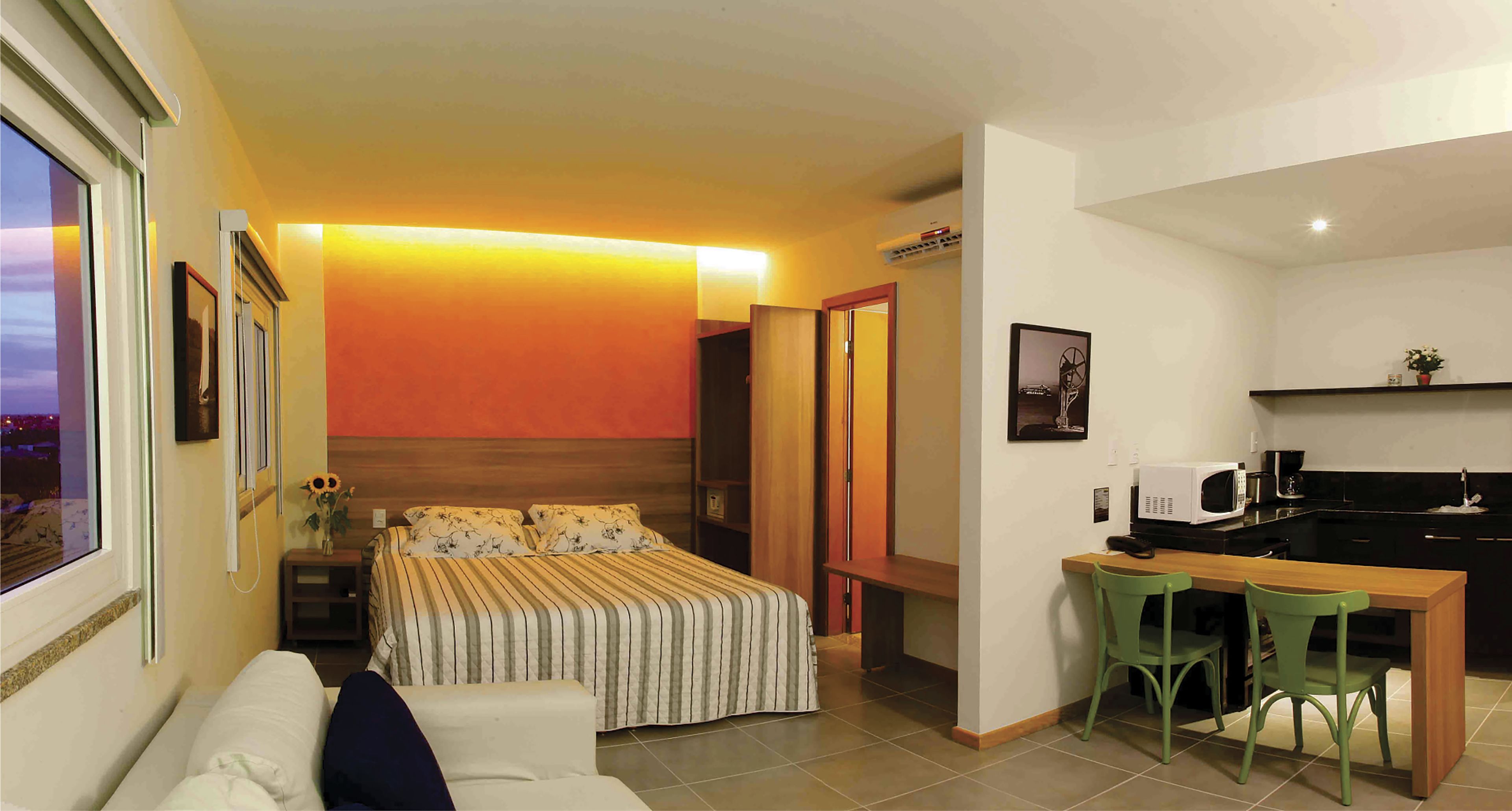 A compact hotel room with a bed, bedside table, and a small kitchenette.