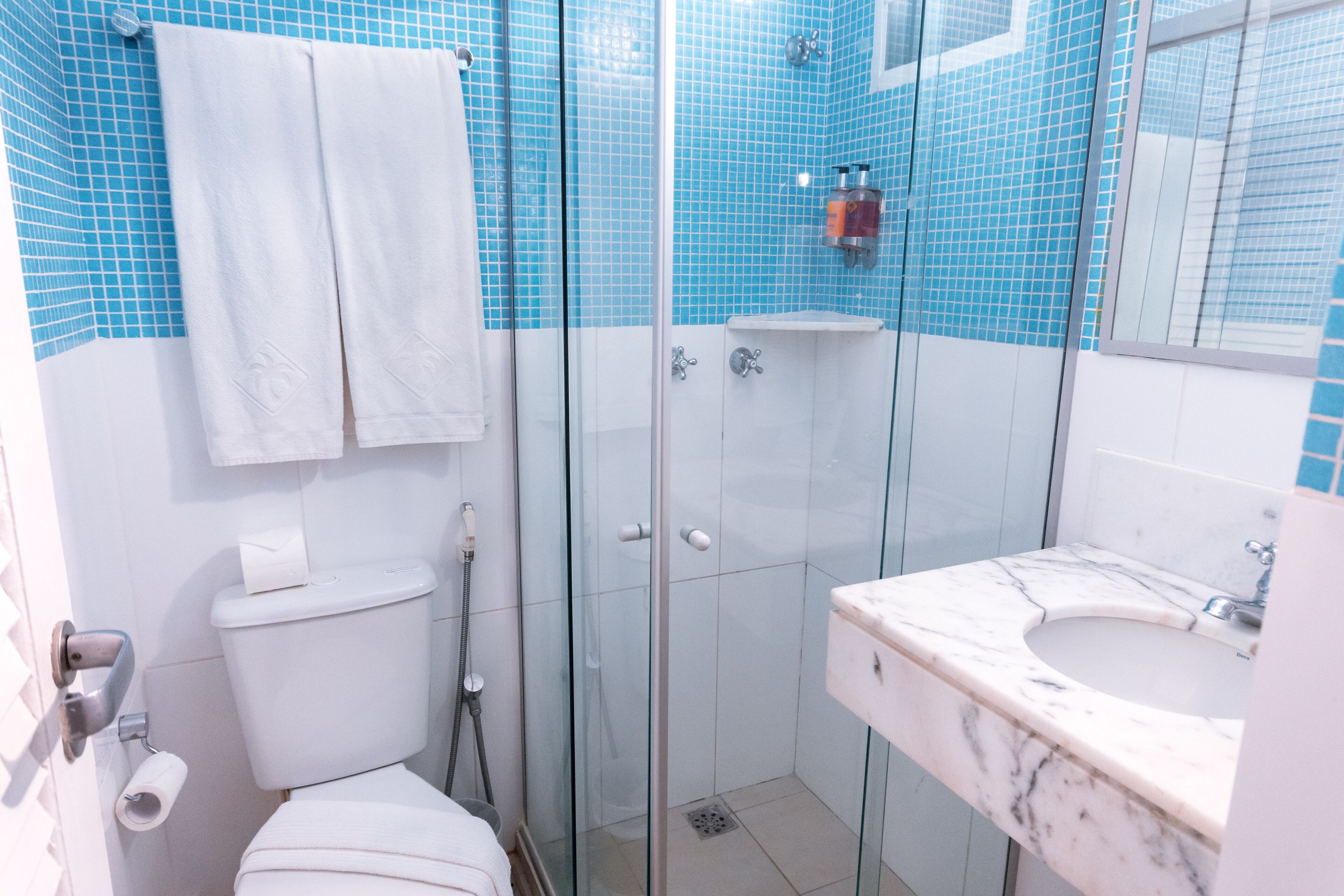 Un baño con cabina de ducha de vidrio, inodoro blanco y lavamanos de mármol.