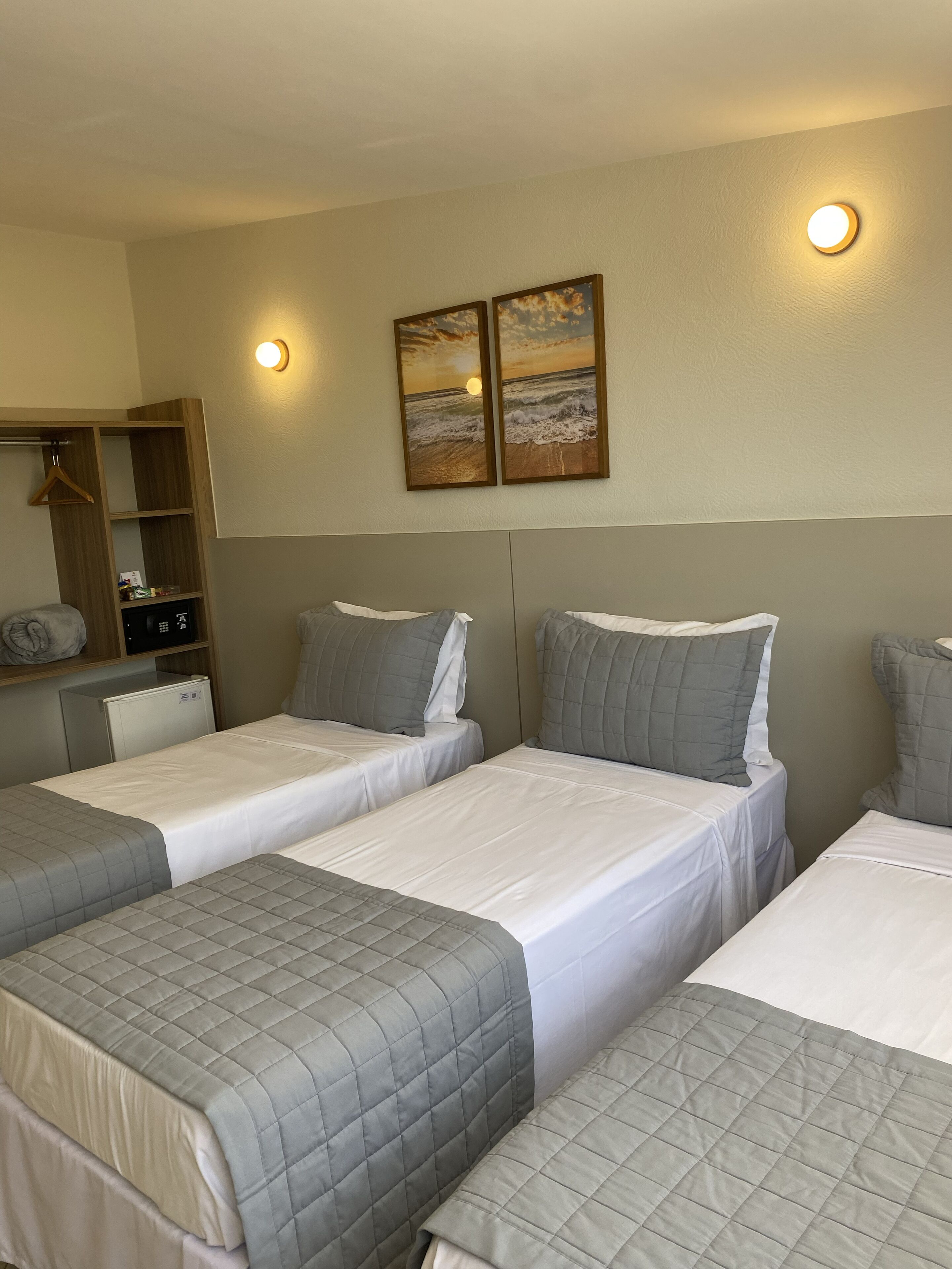 A hotel room with three beds, a wardrobe, and two wall-mounted picture frames.