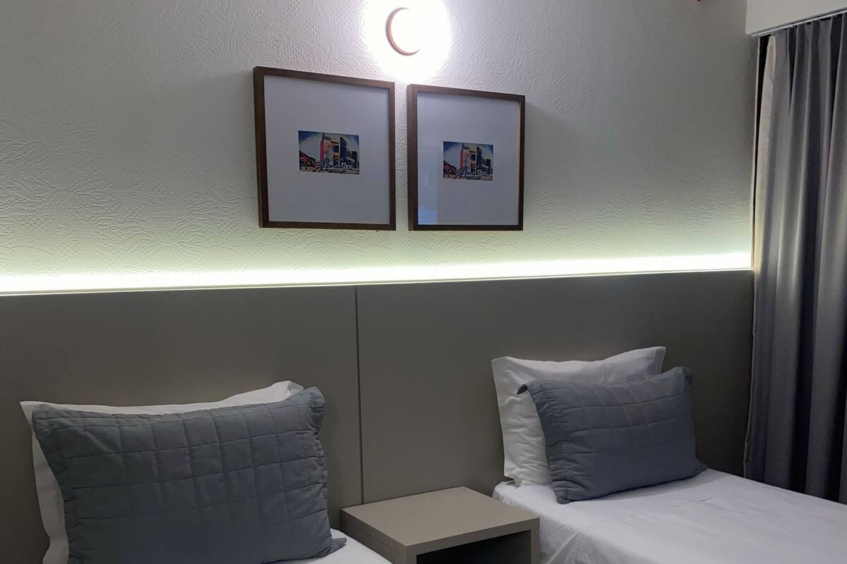 A hotel room with two single beds, a nightstand, and a wall-mounted light fixture.