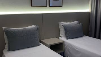 Una habitación de hotel con dos camas individuales, una mesita de noche y una lámpara fijada a la pared.