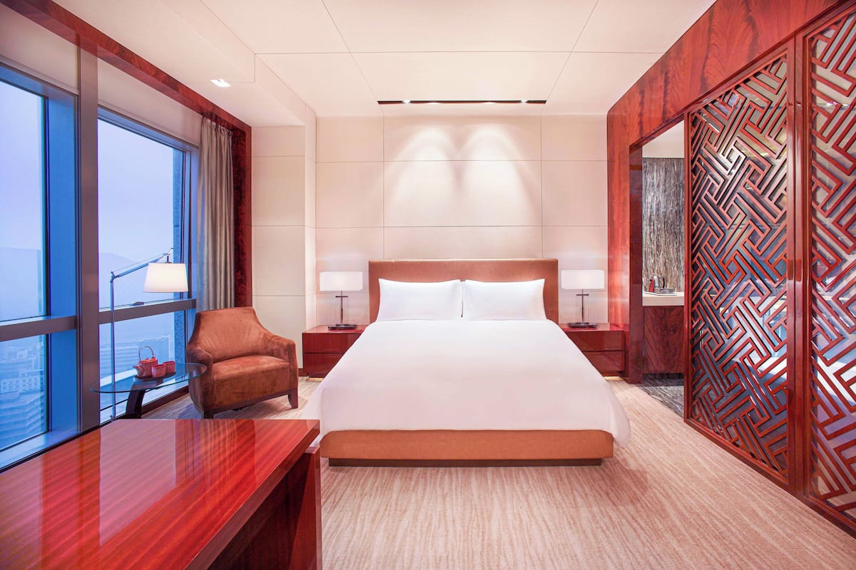A hotel room with a large bed, two bedside tables, a chair, a desk, and a large window with a view.