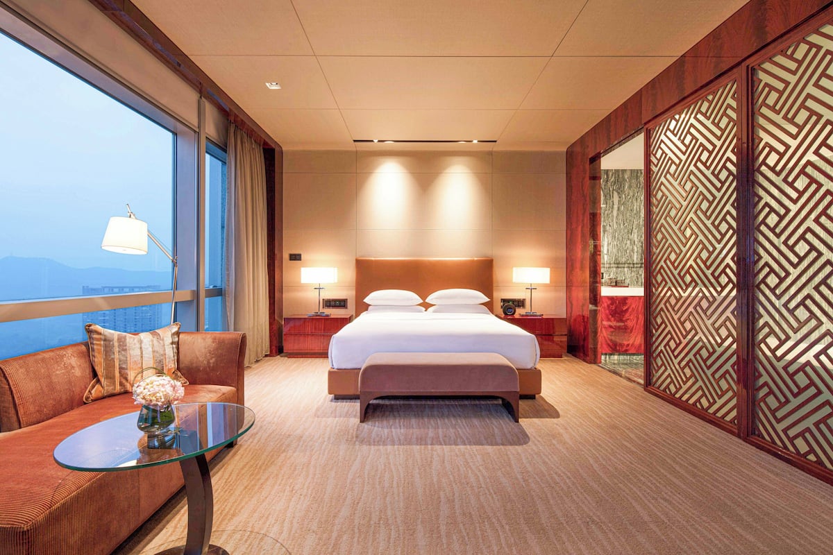A hotel room with a large bed, a glass table, a sofa, and a view of the city.