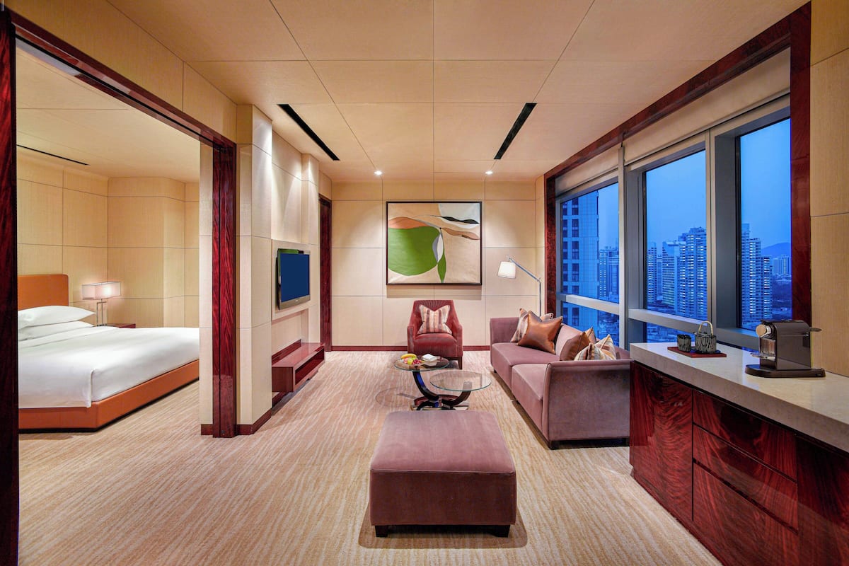 A hotel room with a bed, a sofa, an ottoman, a coffee machine, and a city view.