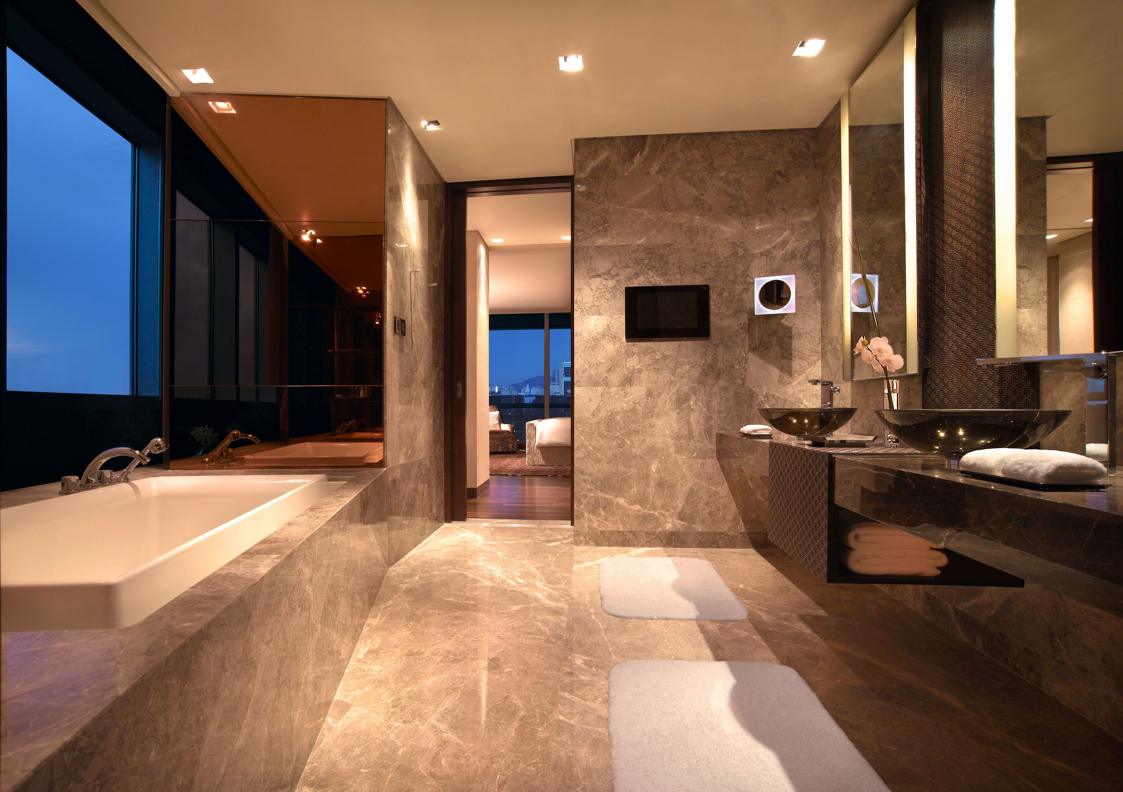 Ein modernes Badezimmer mit einer großen Badewanne, einem Waschbecken und einem Spiegel. Handtücher und ein Fenster mit Blick auf die Stadt vorhanden.