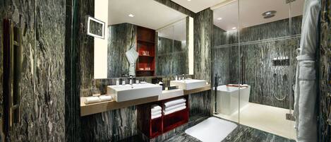 A modern bathroom with marble walls, dual sinks, a glass shower enclosure, and a red vanity.