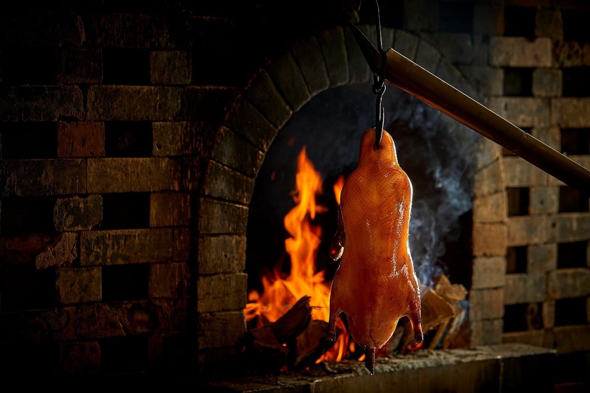 A roasted pig hanging over a brick oven with flames.