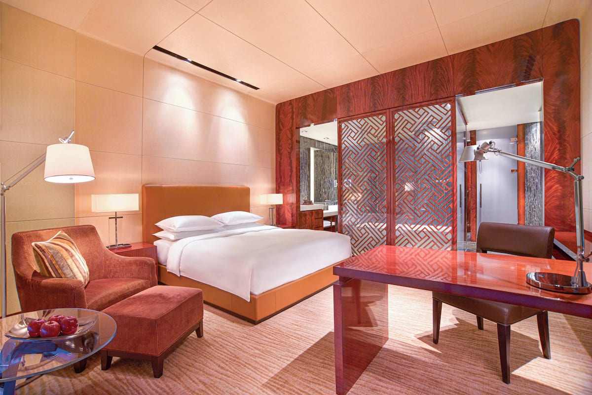 A hotel room with a bed, a desk, a chair, a lamp, and a decorative screen.
