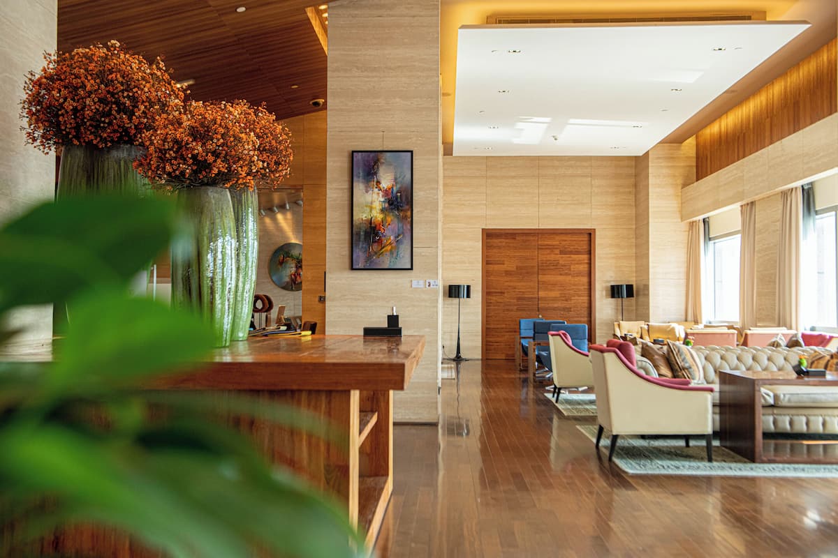 A spacious lobby with a wooden reception desk, a sofa set, and large windows.